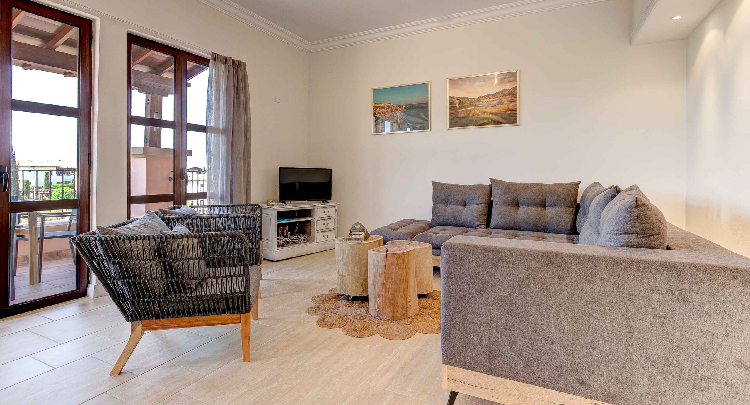 Living area of Apartment APE11 on Aphrodite Hills - showing large sofa, and corner unit with TV and doors opening to balcony.