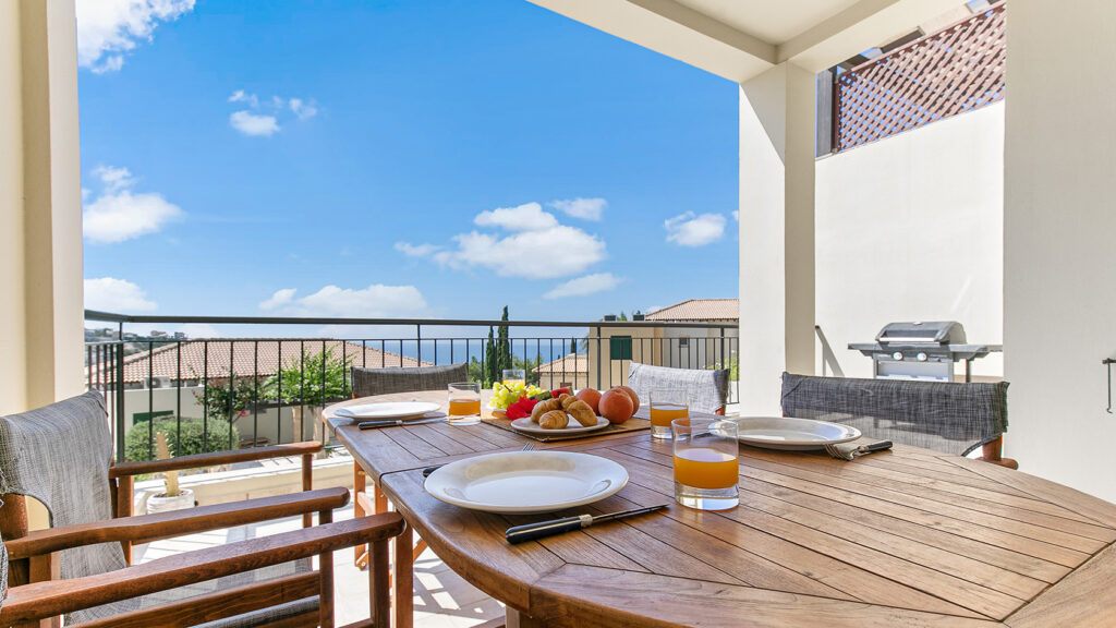 View of breakfast set up with food on outside dining table, balcony at Junior Villa Q3. Blue skies and clouds. Presented by Aphroditerentals.com