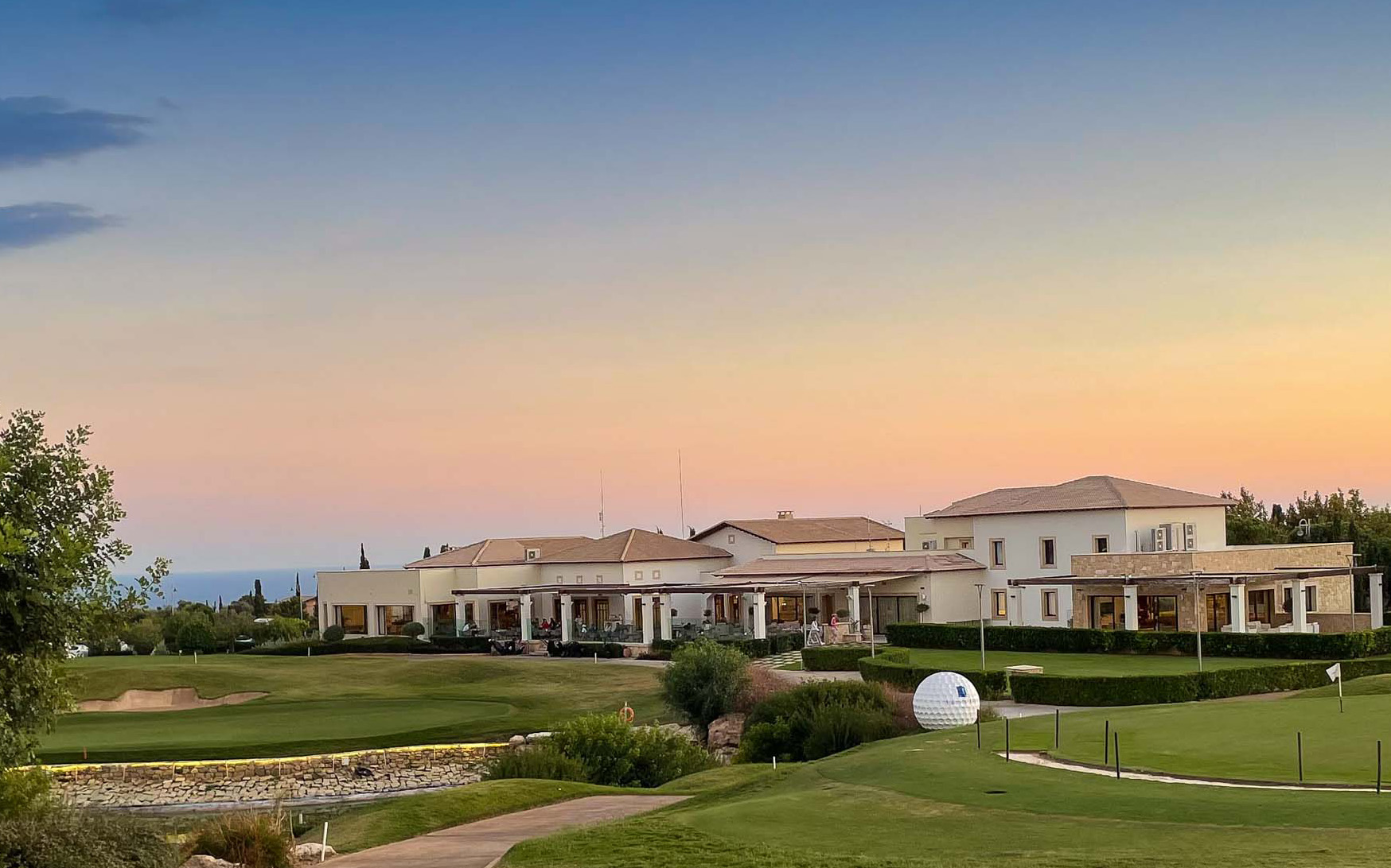 View of the front of the Golf Clubhouse restaurant at Aphrodite Hills Resort, looking over the 18th lake and green, with sunset in the background. Cyprus.