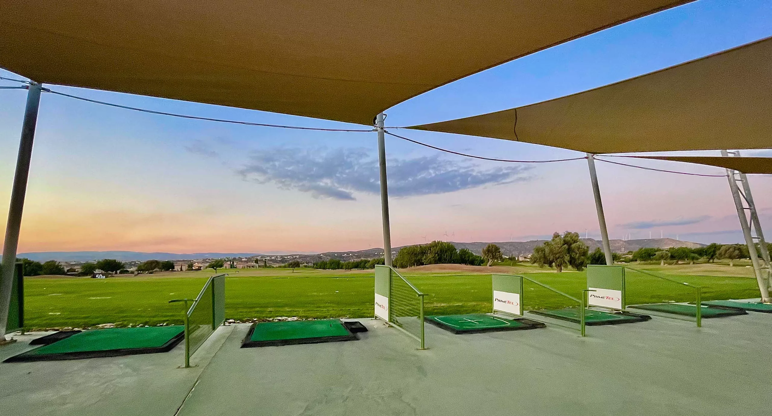 Driving range bays, with shade ports, looking over the driving range out to sunset at Aphrodite Hills PGA National Golf Course.