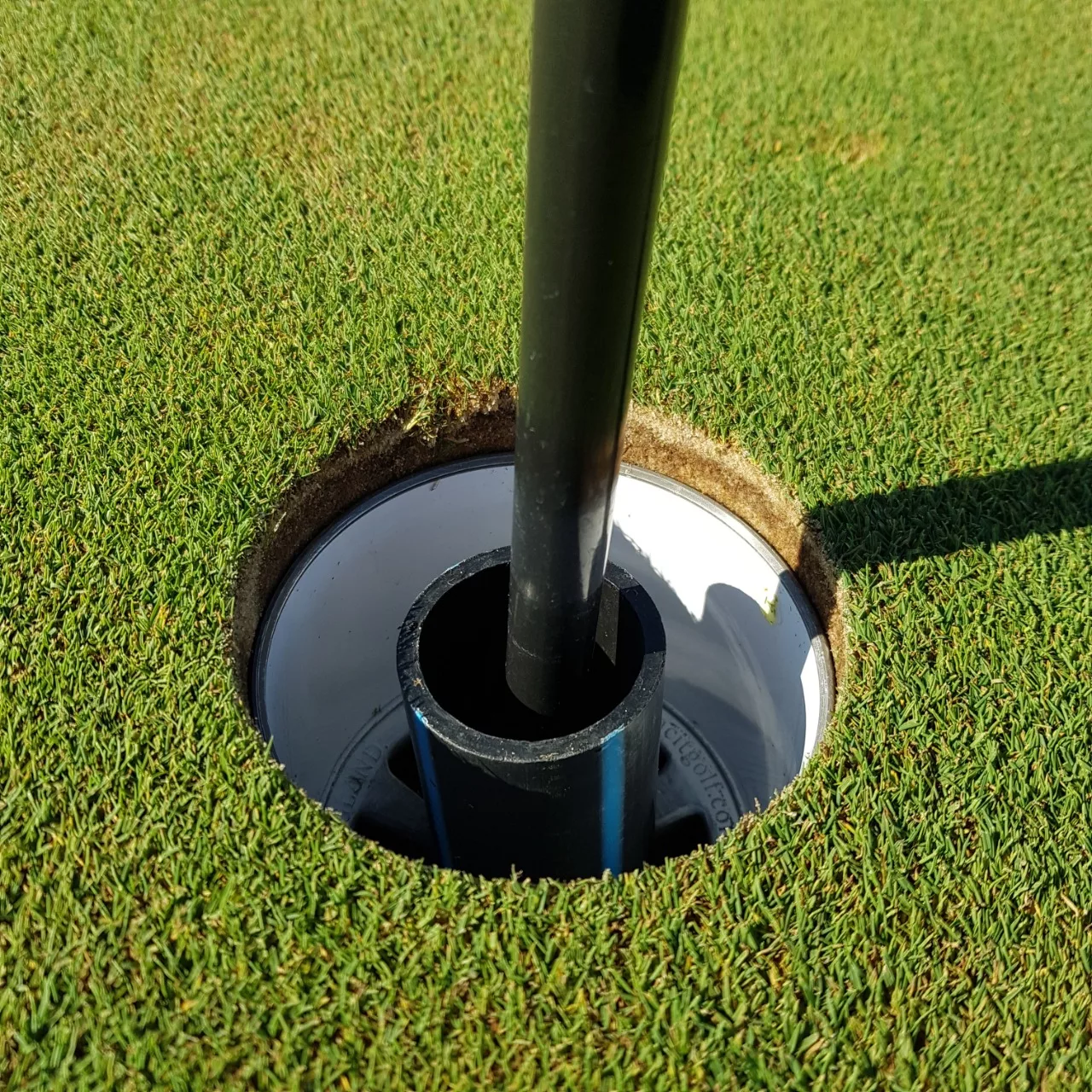 Looking down into a golf hole, with the flag post sticking out, surrounded by green grass.
