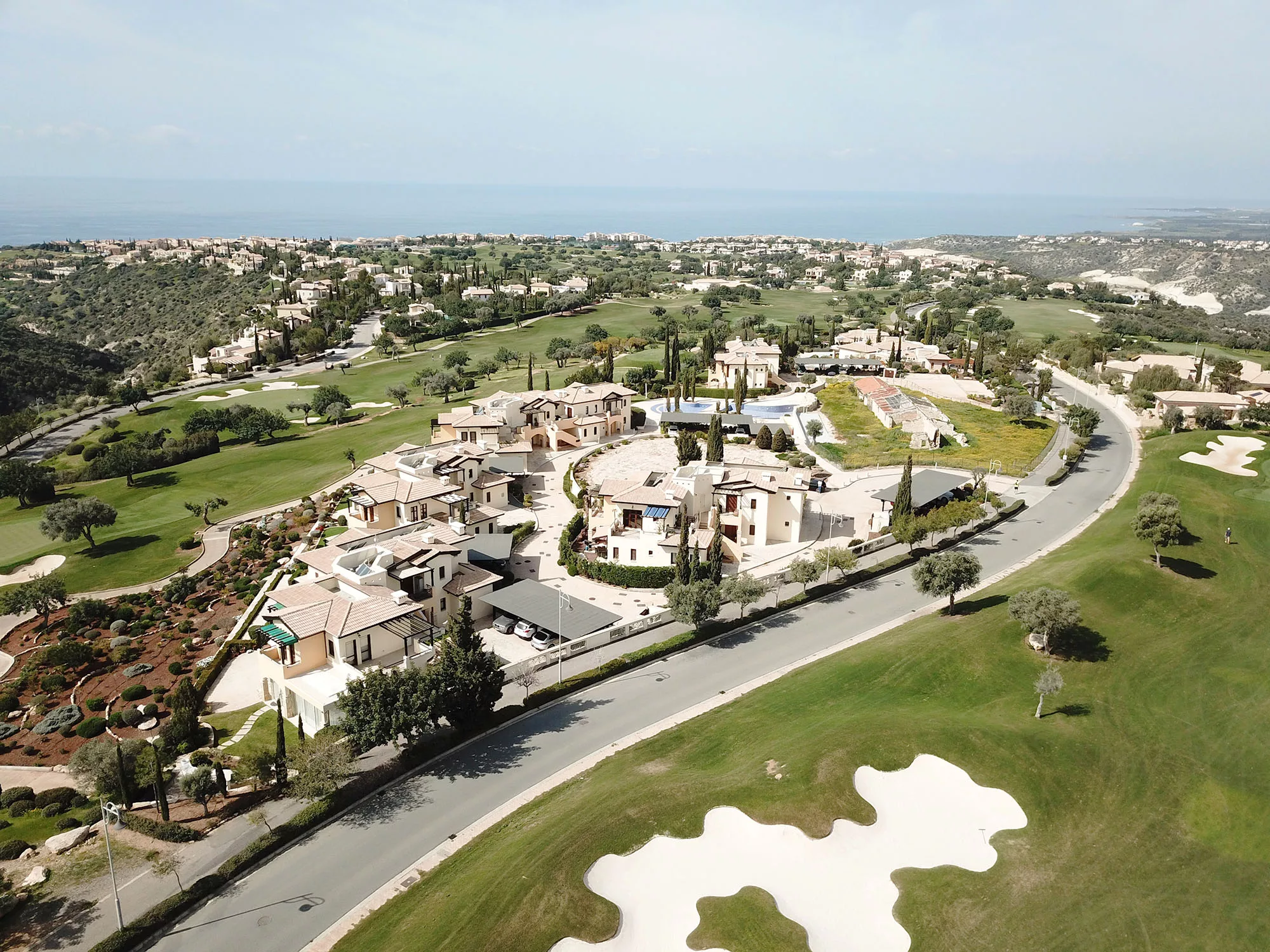 Aerial view of Orpheus Village and golf course holes on Aphrodite Hills PGA National course, looking out to coast and Mediterranean. Properties around resort visable.