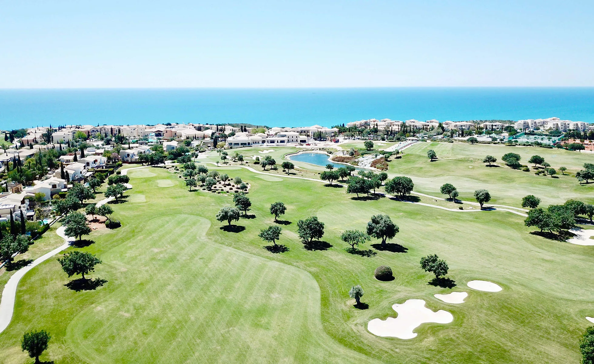 Aerial view of the 1st, 10th and 18th holes at Aphrodite Hills resort, with properties surrounding and Mediterranean Sea in the background.