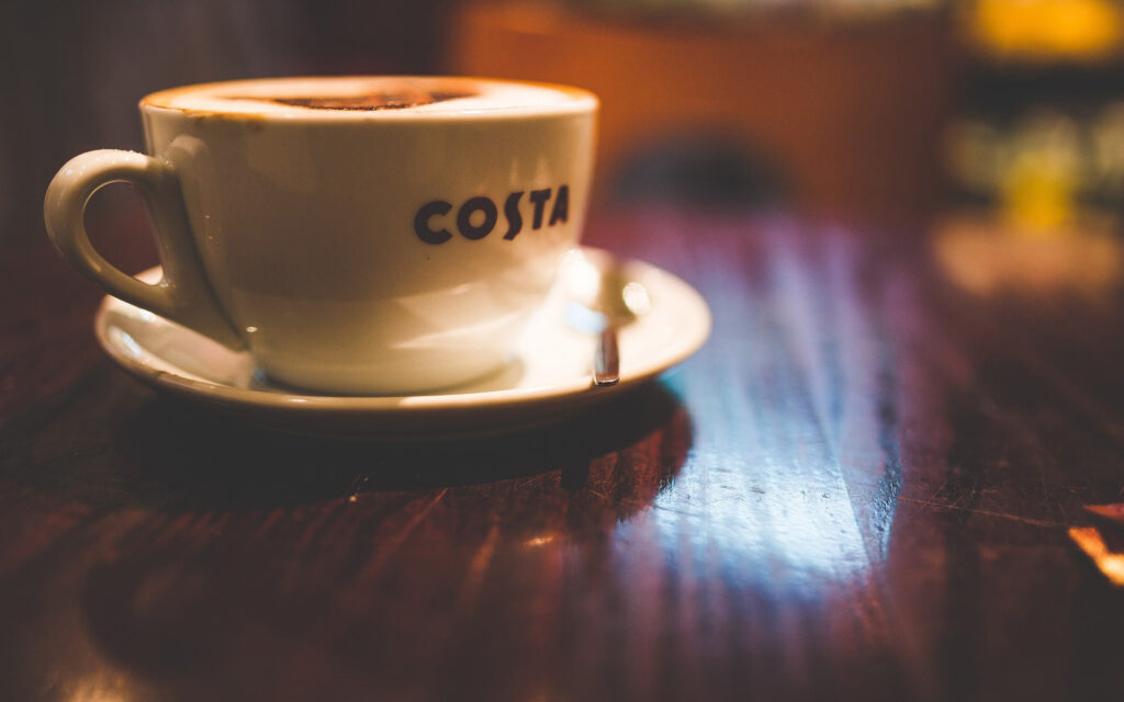 Costa Coffee cup, full, sitting on a table.