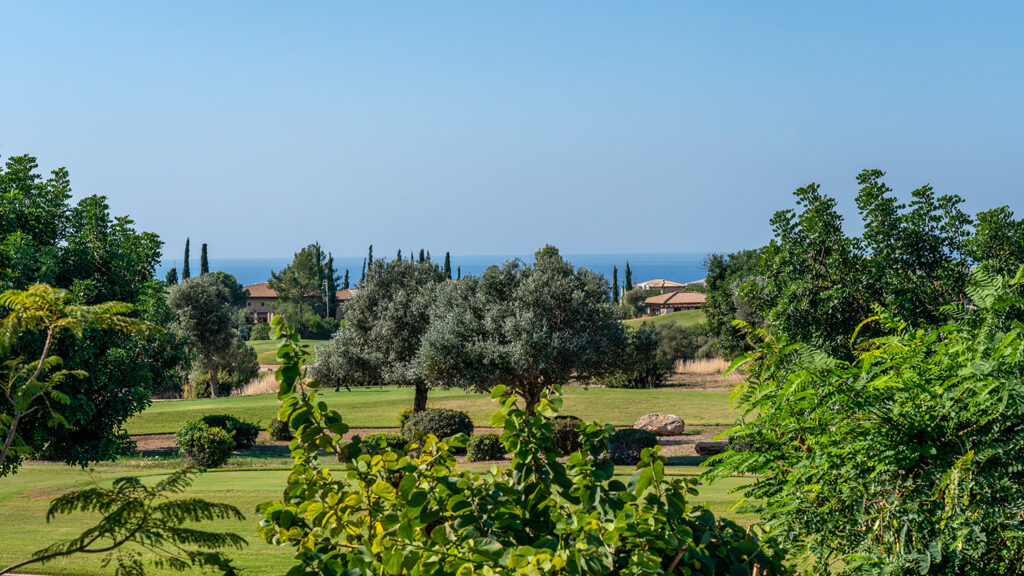 Looking over bushes and trees through Aphrodite Hills Golf Course, with distant views of the Mediterranean Sea.