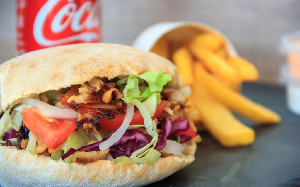 Photo of a kebab with salad, chips and can of coke.