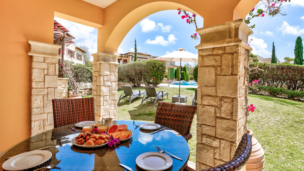 Breakfast set up on outside dining table overlooking garden out to communal pool on Theseus Village, Aphrodite Hills Resort, Cyprus.