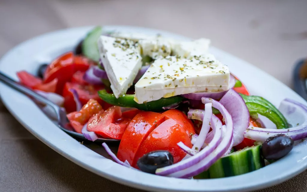 Photo of a Greek Salad in a dish, showing feta, tomato, onions, olives and cucumber.