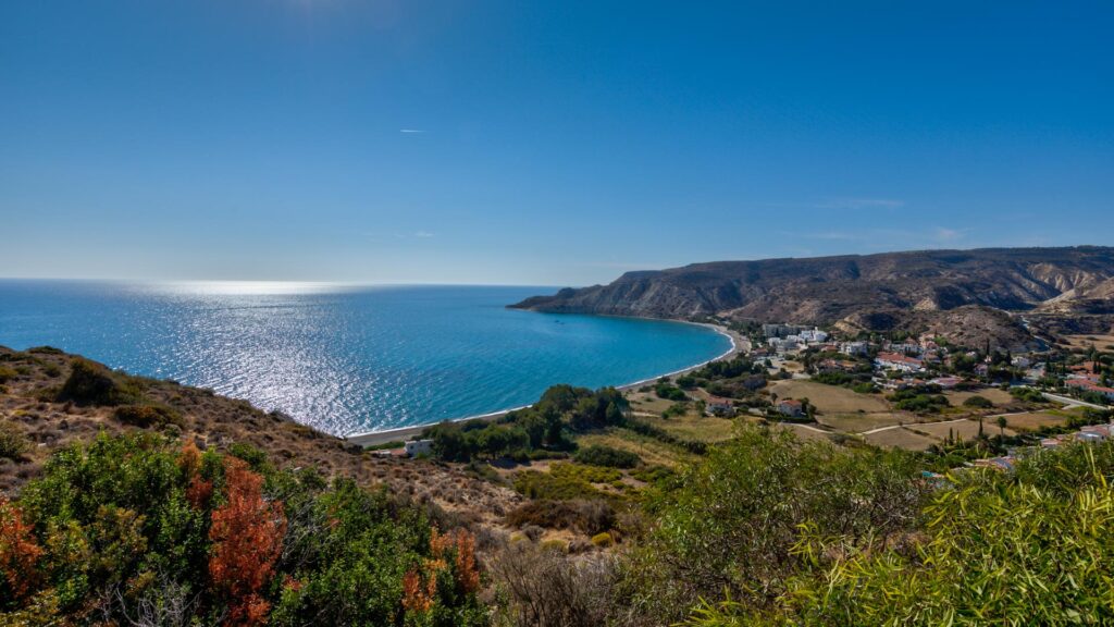 View looking down from a hillside at Pissouri Bay - large bay with fields, trees and houses on the flat, and cliffed edges, showing the Mediterranean Sea.