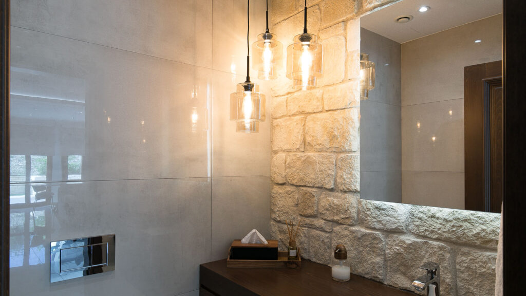 Corner of Bathroom in Villa Agapi on Aphrodite Hills; stone wall, rear lit mirror and contemporary light fixtures.
