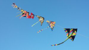 A line of kites flying against blue sky, each with different designs.