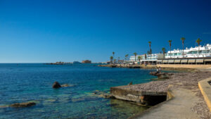 Looking over sea to Paphos Harbour - buildings of restaurants and cafes in the background, as well as Paphos Medieval Fort.
