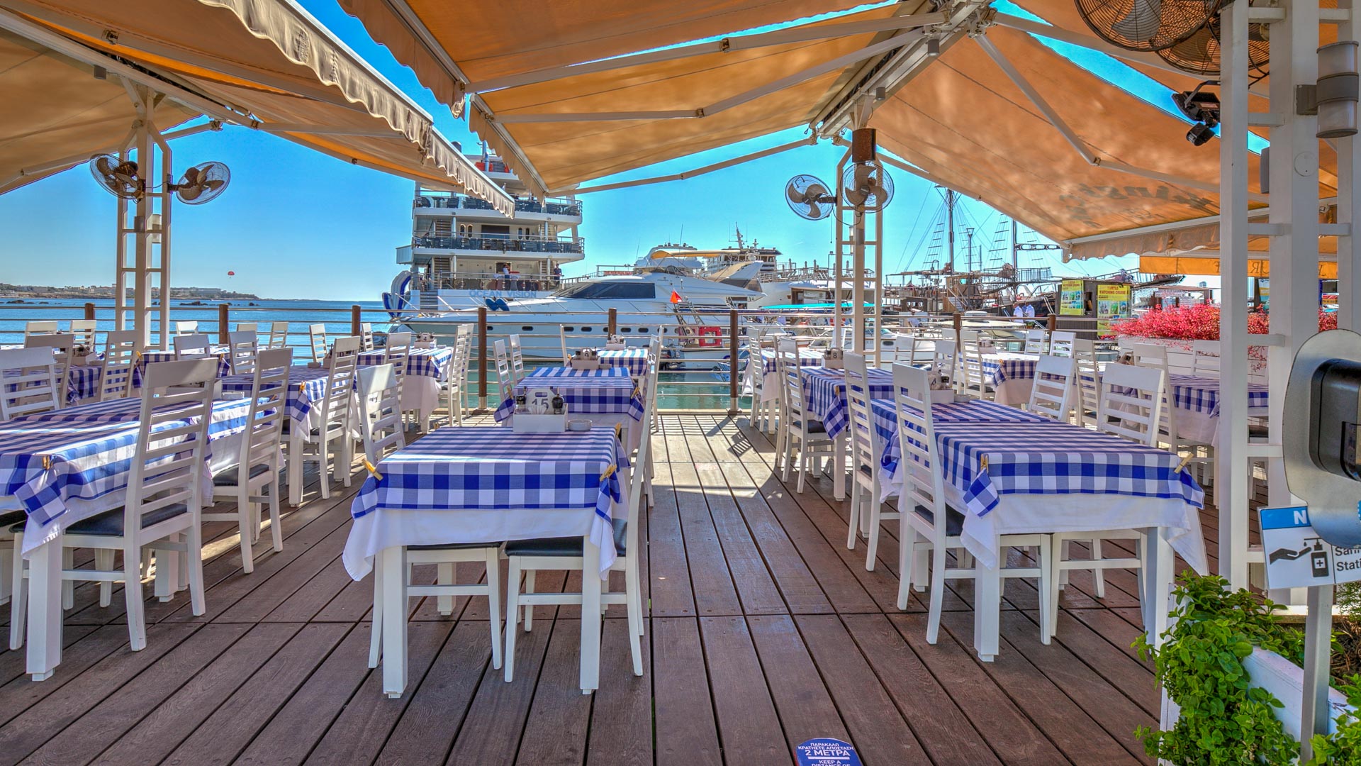 Decked restaurant space with tables set up, overlooking the boats on Paphos harbour.