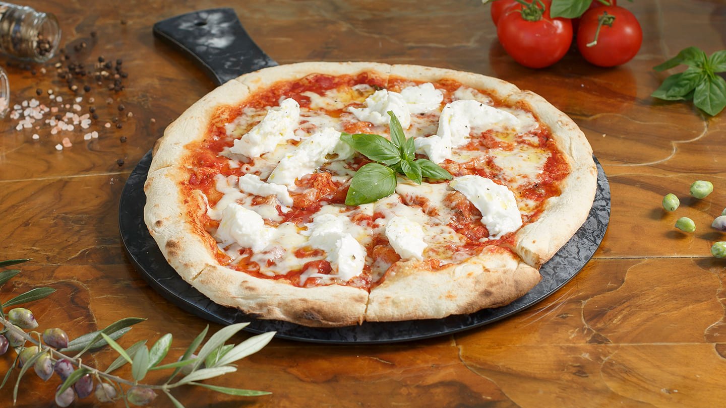 Photograph of a homemade pizza on a pizza slate, on wooden table.