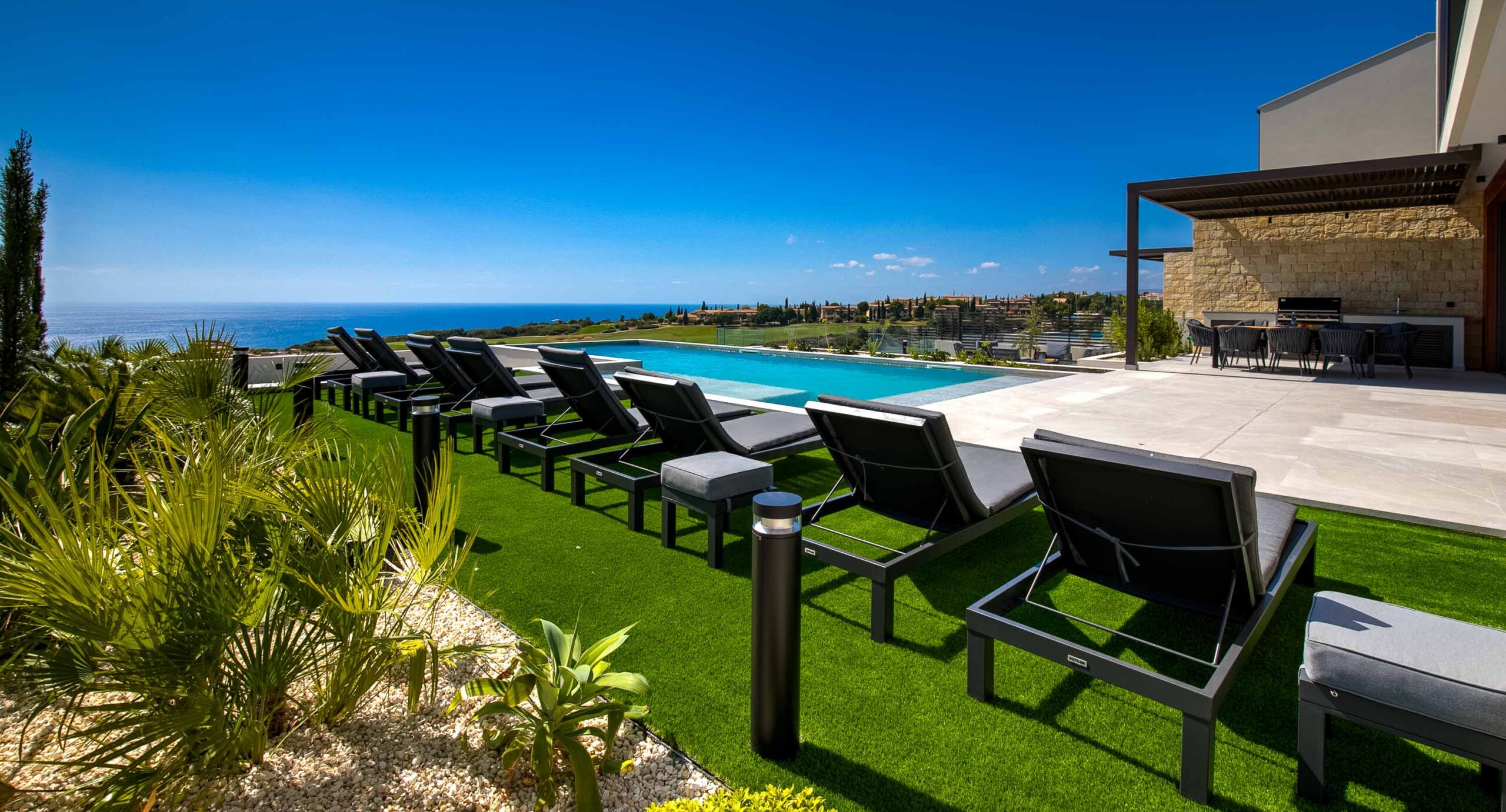 Photo of Villa 286 on Aphrodite Hills - side view looking on to the pool and outside terrace, golf & sea view, with sun beds in the foreground.